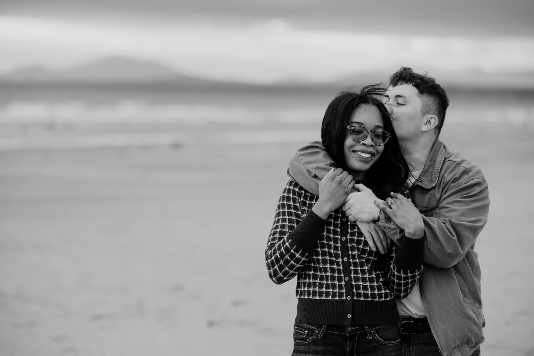 Black-and-white portrait of a couple embracing on the beach after their engagement