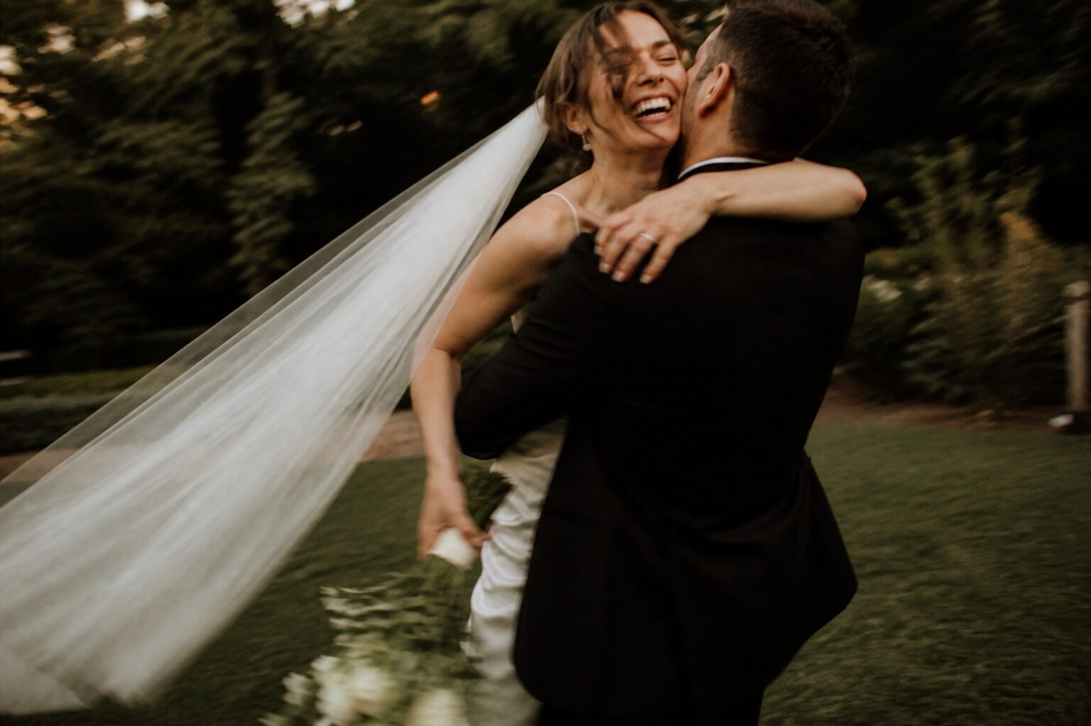 Bride laughing as she is lifted during a woodland wedding celebration