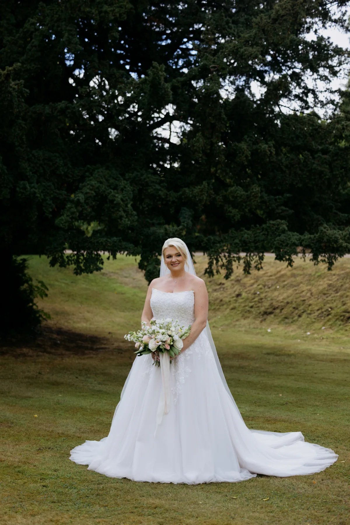 Bride holding her bouquet beneath a tree at Clearwell Castle