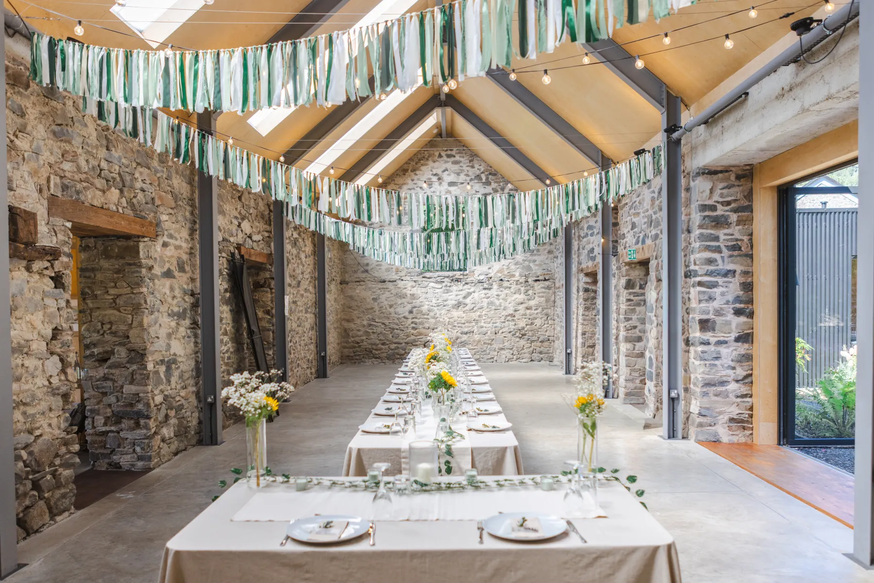 Wedding breakfast tables beneath ribbon garlands inside Nant y Walch Barn